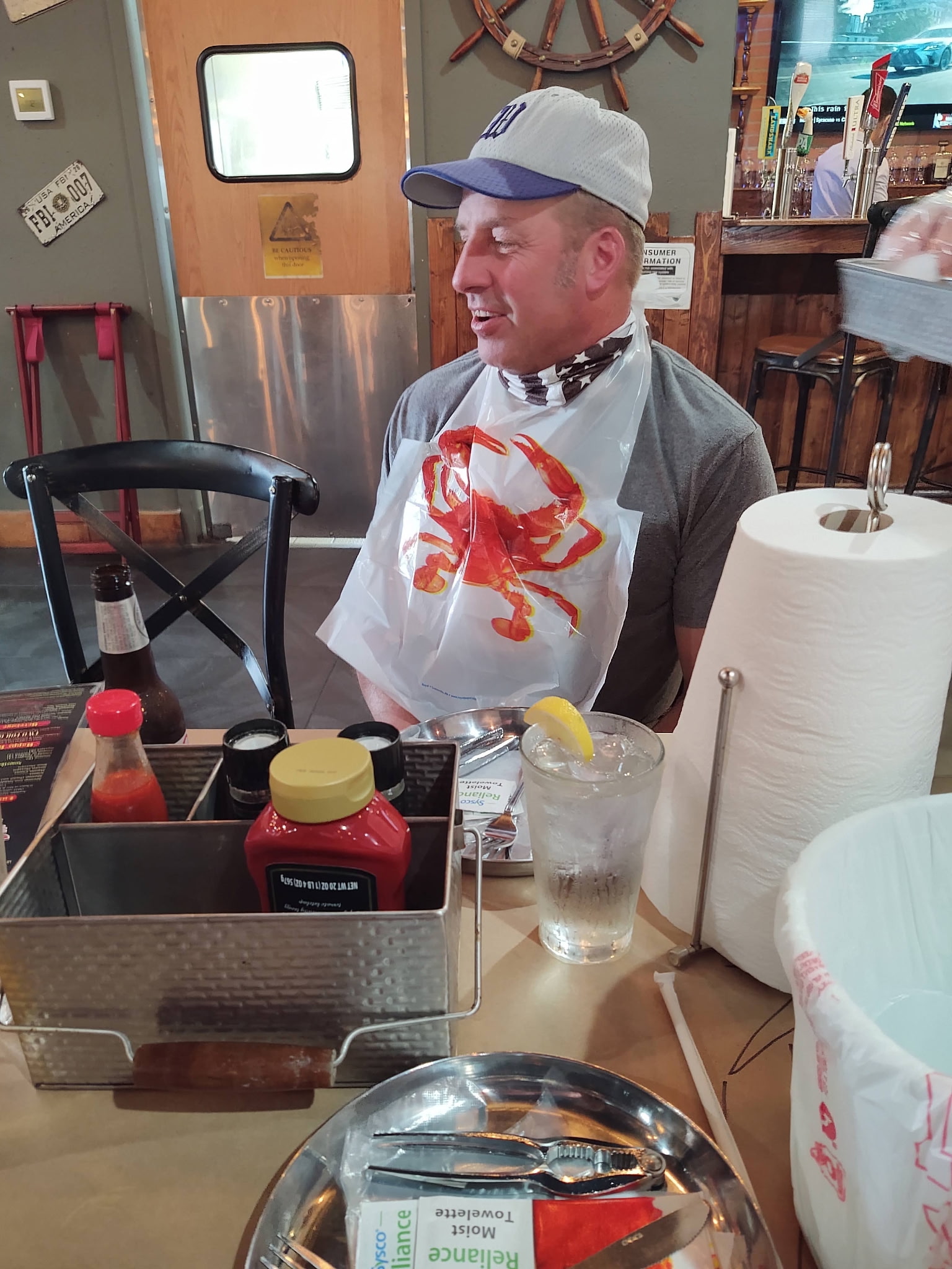 A man at a restaurant table wearing a baseball cap and a lobster bib